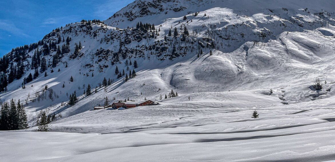 Verschneite Winterlandschaft in den Bergen mit einer Alp im Hintergrund. | © Silvretta Montafon - Vanessa Strauch