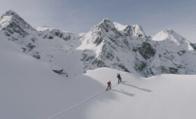 Zwei Männer durchqueren ein Schneefeld in der Silvretta Montafon mit Ski auf dem Rücken