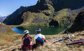 Ein Paar sitzt an einem See in der Silvretta Montafon mit den Bikes daneben