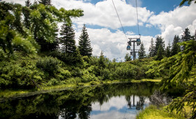 Die Grasjoch Bahn mit Gondeln über einem kleinen See zwischen Bäumen im Sommer 