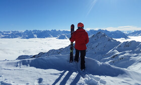 Eine Skifahrerin steht neben der Piste und blickt auf das Nebelmeer und das Bergpanorama