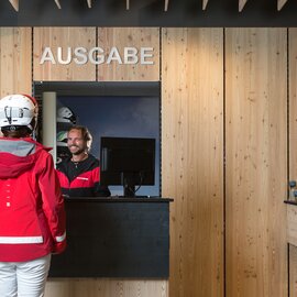 Eine Skifahrerin steht vor dem Ausgabe-Fenster im Intersport St. Gallenkirch und wird von einem Mitarbeiter bedient
