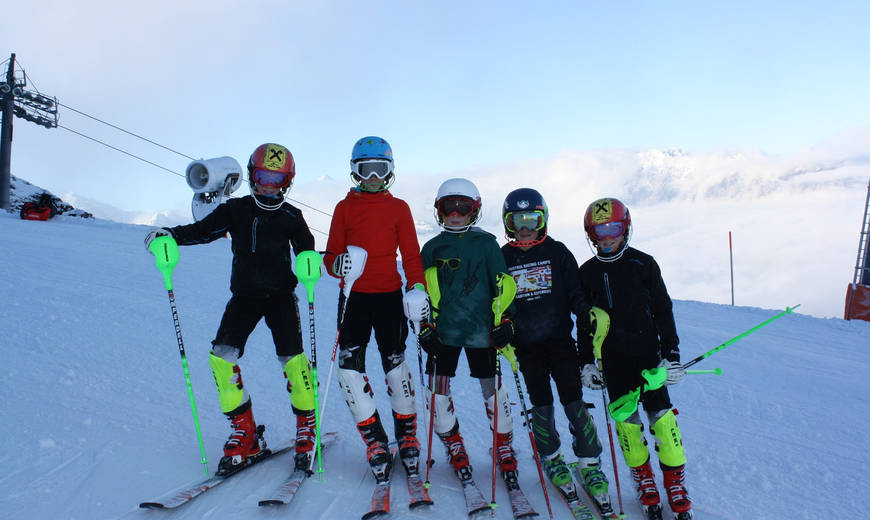 Fünf junge Rennfahrer stehen nebeneinander mit Skiausrüstung auf der Piste