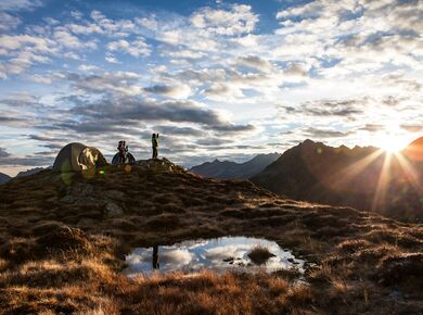 Zwei Personen stehen vor dem Zelt und genießen den Sonnenaufgang in den Bergen