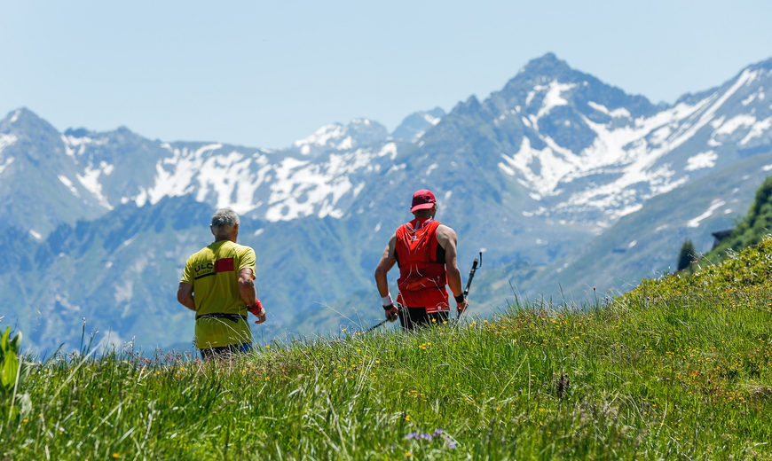 Zwei Teilnehmer des Montafon Totale Trails rennen über die Wiese mit dem Rücken zur Kamera und dem Gesicht zur Sonne