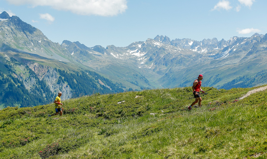 Zwei Teilnehmer des Montafon Totale Trails rennen über eine Wiese mit den Bergen im Hintergrund