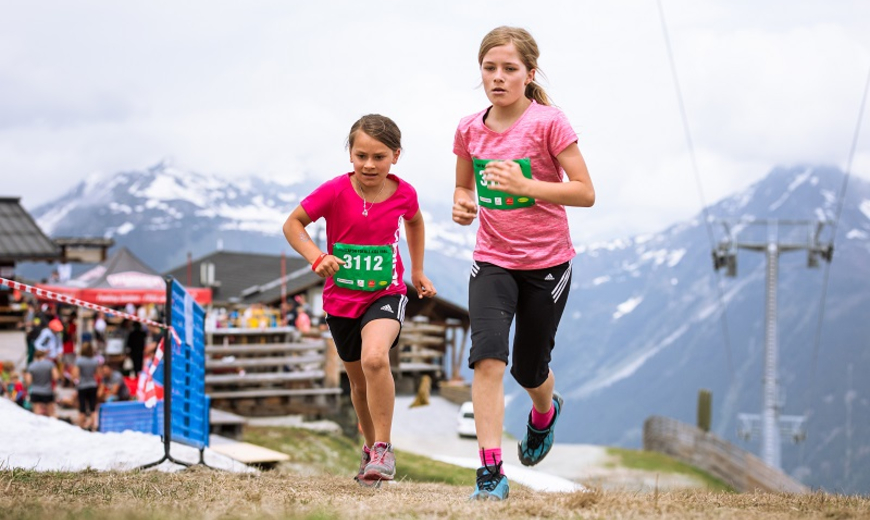 Zwei Mädchen im roten und pinken T-Shirt rennen nebeneinander den Hügel hoch
