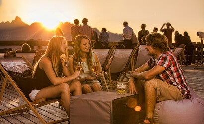Drei Freunde trinken und lachen zusammen auf der Kapellrestaurant Terasse im Sonnenuntergang