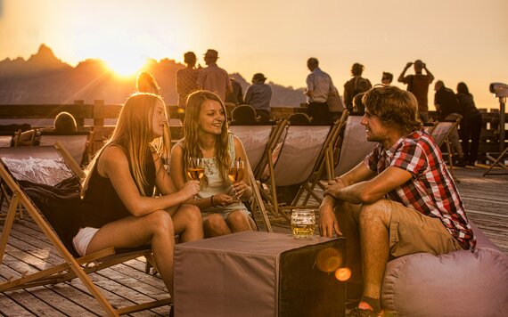 Drei Freunde trinken und lachen zusammen auf der Kapellrestaurant Terasse im Sonnenuntergang
