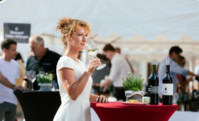 Eine Frau steht an einem Stehtisch beim Weinfest und probiert einen Weißwein