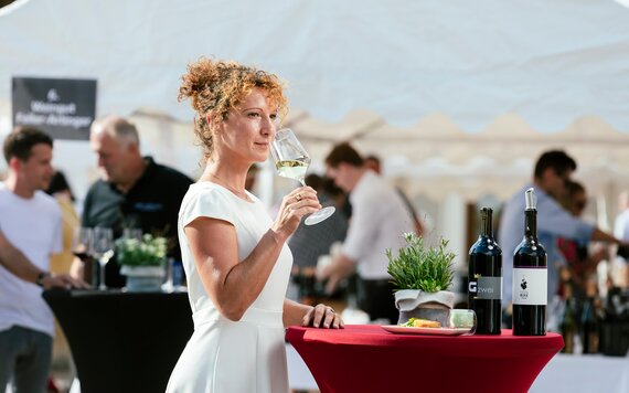 Eine Frau steht an einem Stehtisch beim Weinfest und probiert einen Weißwein
