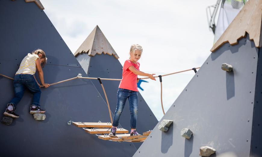 Zwei Kinder klettern und balancieren den Hindernisse am Spielplatz auf dem Abenteuerberg Hochjoch entlang
