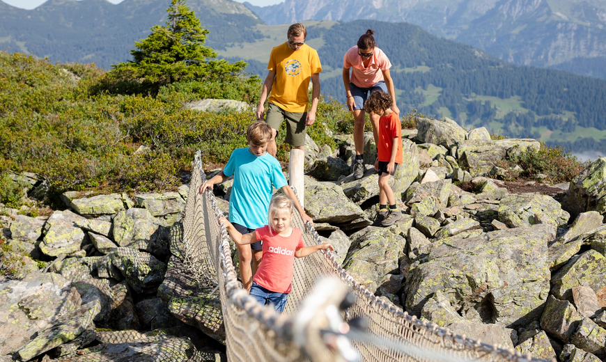 Eine Familie läuft auf dem Wanderweg über die Hängebrucke am Abenteuerberg Hochjoch