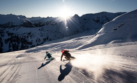 Zwei Skifahrer gleiten über die frischen Pisten am Morgen mit Bergpanorama im Hintergrund