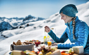 Eine Frau sitzt an einem Tisch in den Bergen im Winter und vor ihr ist ein Frühstücksbuffet aufgebaut