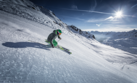Ein Skifahrer saust die frisch präparierte Piste mit Bergpanorama und Sonnenschein im Hintergrund hinunter