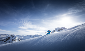 Ein Skifahrer zieht eine Kurve über den Hang und die frische Piste mit Bergpanorama im Hintergrund