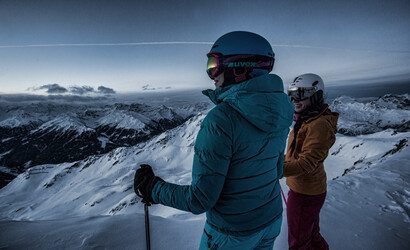 Zwei Personen in Skikleidung genießen die Ruhe am Morgen und die Aussicht auf das Bergpanorama