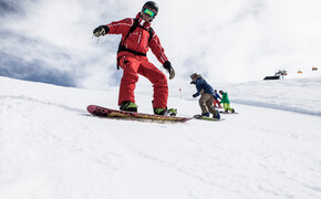 Ein Snowboardlehrer fährt langsam mit einer Gruppe von Snowboardern die Piste hinunter