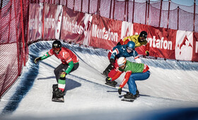 Vier Snowboard Cross Teilnehmer lehnen in die Kurve der Rennstrecke
