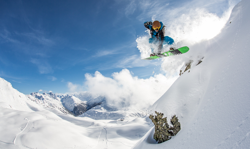 Ein Snowboarder springt eine Cliff hinab in den Tiefschnee und macht einen Trick