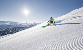 Ein Skifahrer in gelb-blauem Skianzug saust die frische Piste im Sonnenschein hinunter
