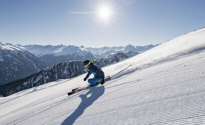 Ein Skifahrer in blauer Skikleidung zieht seine Schwünge auf Ski auf den frisch-präparierten Pisten