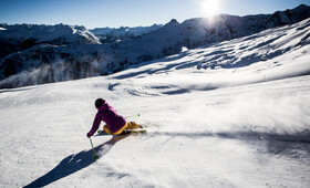 Ein Skifahrer in Skikleidung und Helm saust eine breite Piste im Winter hinunter