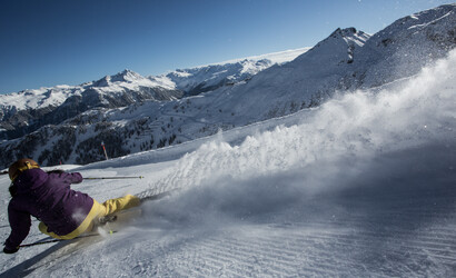 Skifahrer carvt den Hang hinunter und macht eine Schneewolke