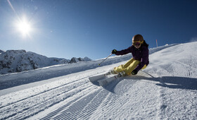 Skifahrer fährt eine Kurve auf der frisch präparierten Piste an einem sonnigen Tag 