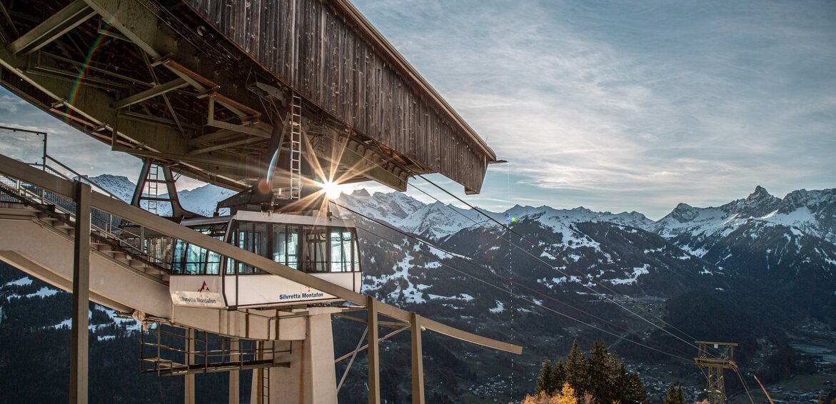 Eine Kabinenbahn fährt in die Bergstation bei Abendsonne und verschneiten Bergspitzen. | © Silvretta Montafon - Frederike Weber
