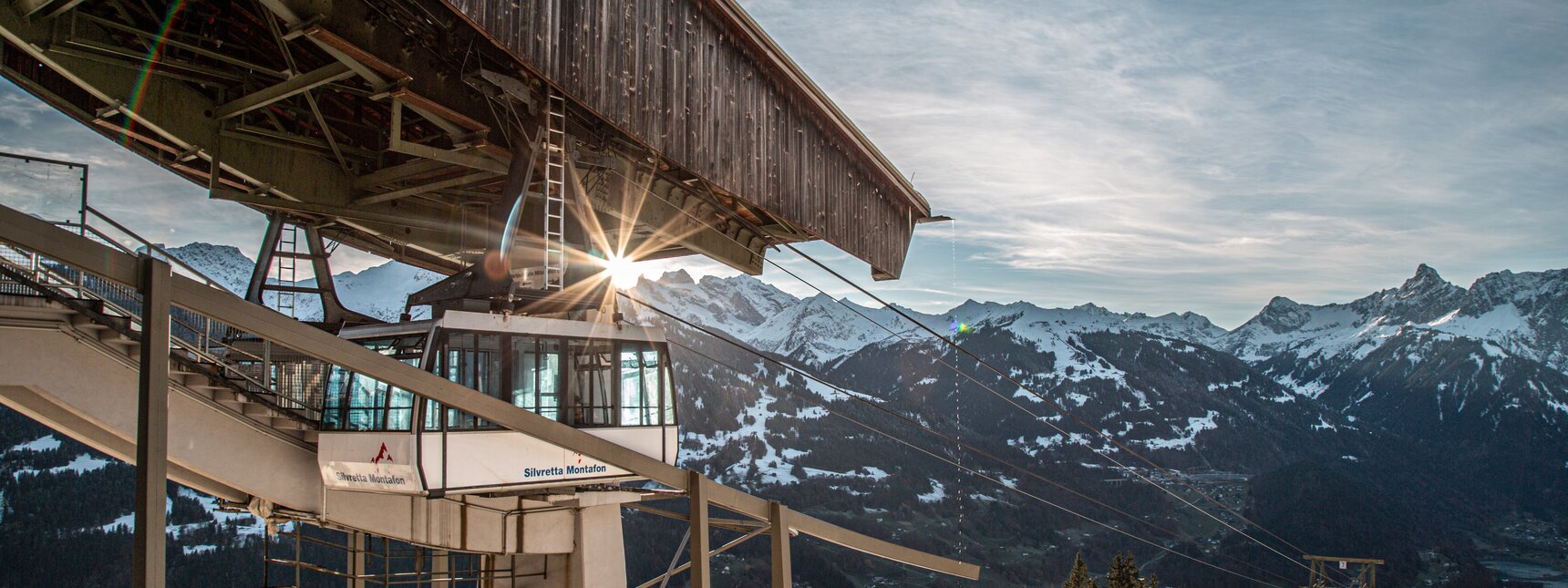 Eine Kabinenbahn fährt in die Bergstation bei Abendsonne und verschneiten Bergspitzen. | © Silvretta Montafon - Frederike Weber