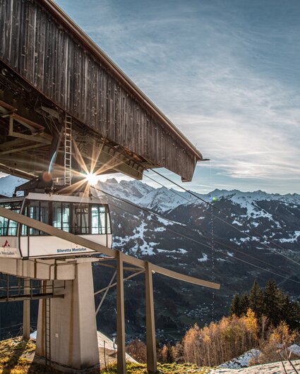 Eine Kabinenbahn fährt in die Bergstation bei Abendsonne und verschneiten Bergspitzen. | © Silvretta Montafon - Frederike Weber