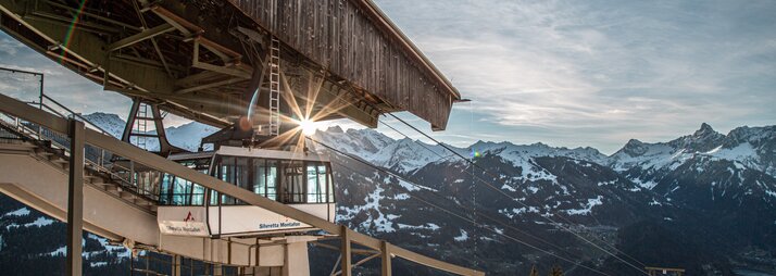 Eine Kabinenbahn fährt in die Bergstation bei Abendsonne und verschneiten Bergspitzen. | © Silvretta Montafon - Frederike Weber