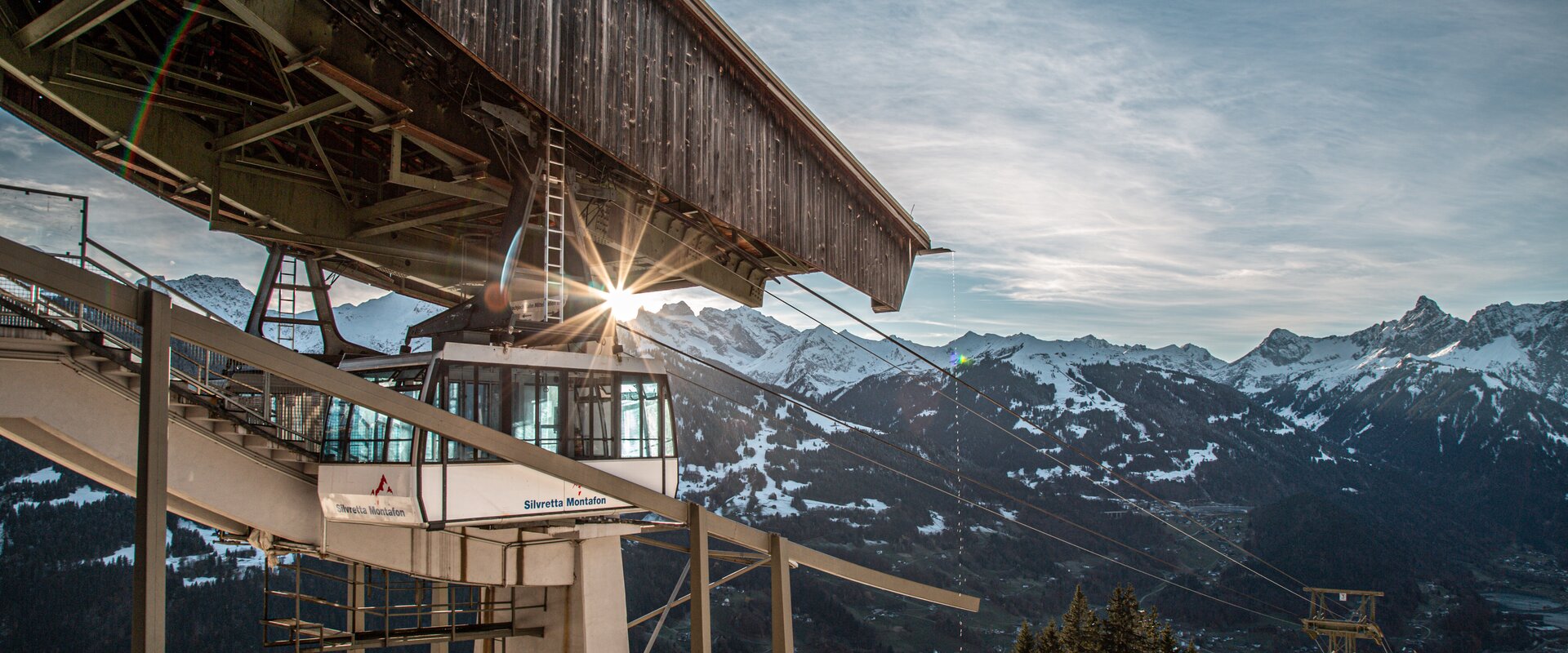 Eine Kabinenbahn fährt in die Bergstation bei Abendsonne und verschneiten Bergspitzen. | © Silvretta Montafon - Frederike Weber