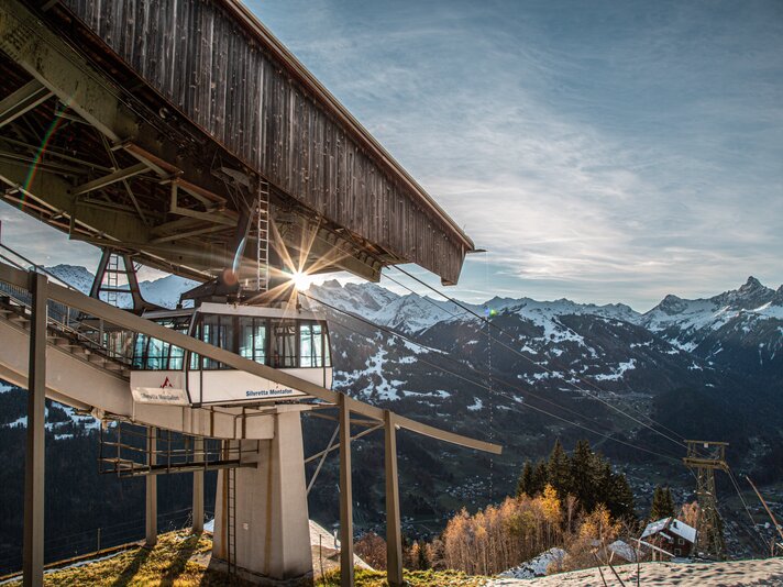 Eine Kabinenbahn fährt in die Bergstation bei Abendsonne und verschneiten Bergspitzen. | © Silvretta Montafon - Frederike Weber