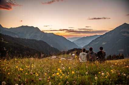 Drei Person sitzen in der Wiese am Berg und genießen das Abendlicht im Bergdorf in der SIlvretta Montafon. | ©  Silvretta Montafon - Friederike Weber
