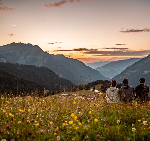 Drei Person sitzen in der Wiese am Berg und genießen das Abendlicht im Bergdorf in der SIlvretta Montafon. | ©  Silvretta Montafon - Friederike Weber