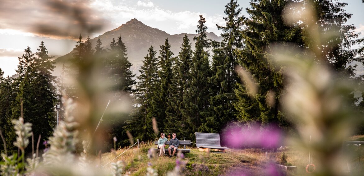 Zwei Personen sitzen auf einer Bank in der Abendsonne am See im Alpendorf Garfrescha. | ©  Silvretta Montafon - Friederike Weber