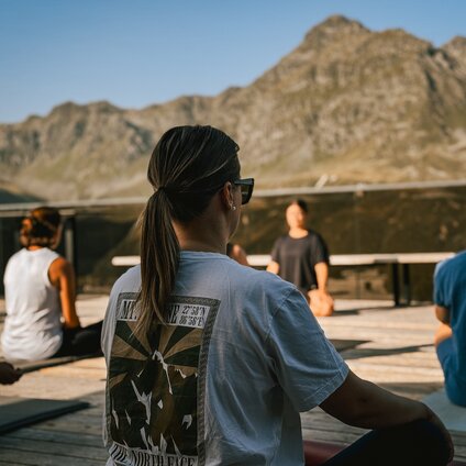 Eine Gruppe von Personen sitzt auf einer Terrasse bei Morgensonne und macht Yoga. | © Silvretta Montafon - Vanessa Strauch