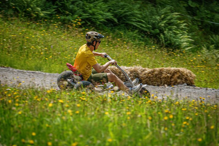 Ein Mann fährt auf einem Mountaincart einen Weg zwischen Bergwiesen entlang. | © Silvretta Montafon - Vanessa Strauch