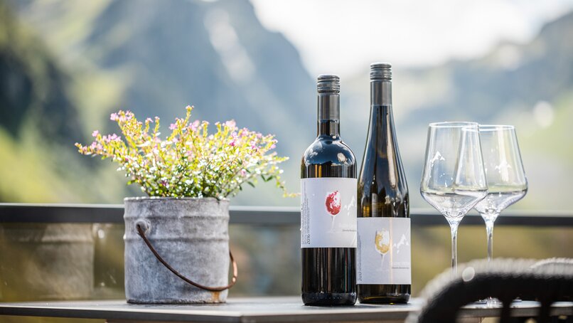 Weingläser und Weinflaschen stehen auf einem Tisch mit einem Blumengesteck. | © Silvretta Montafon - Stefan Kothner