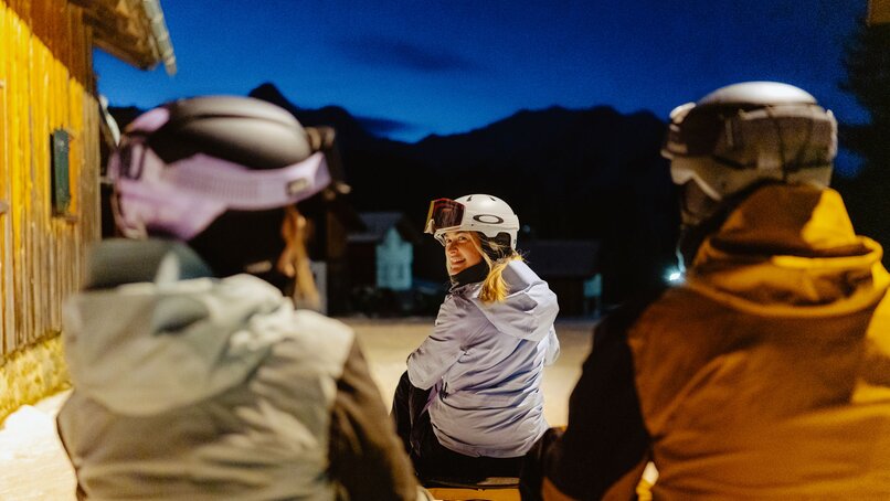 Drei Personen in Skikliedung rodeln auf einem Schlitten am Abend. | © Silvretta Montafon - Marie Schilcher