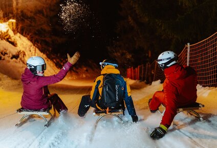 Drei Freunde rodeln auf der Nachtrodelbahn  | © Silvretta Montafon - Marie Schilcher