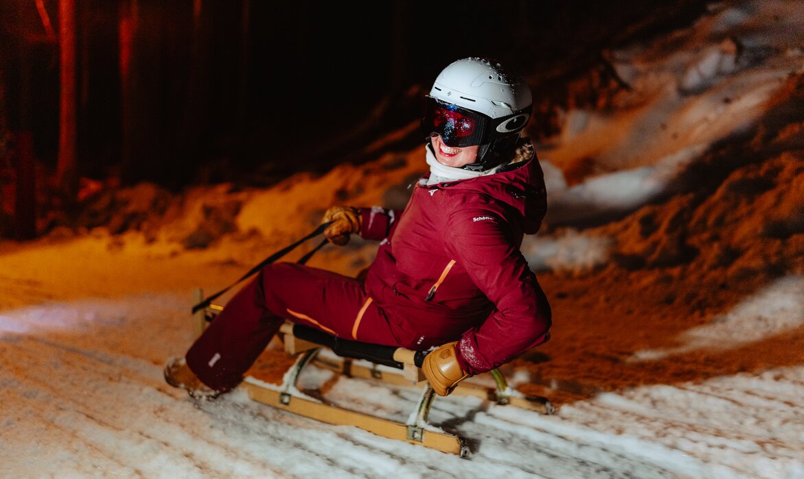Eine Frau rodelt auf einem Schlitten und lacht. | © Silvretta Montafon - Marie Schilcher