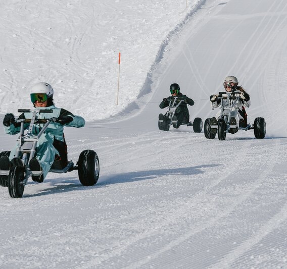 Drei Personen fahren auf einem Mountaincart auf einer Skipiste. | © Silvretta Montafon - Niklas Kirchler