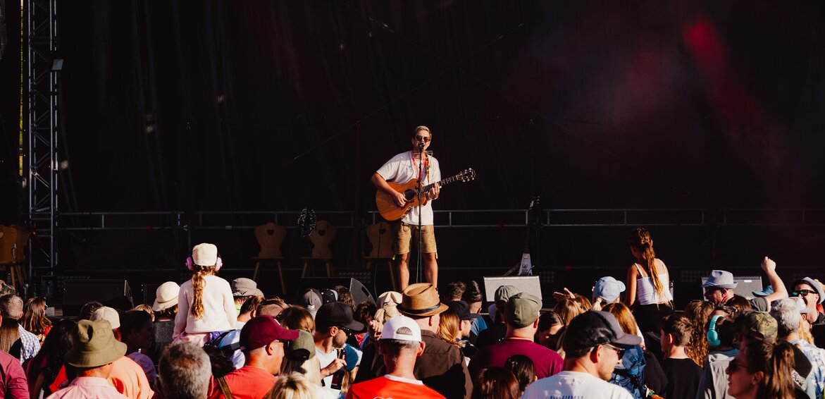 Ein Musiker mit Gitarre auf einer Bühne und eine großes Publikum steht davor. | © Silvretta Montafon - Robin Mayer