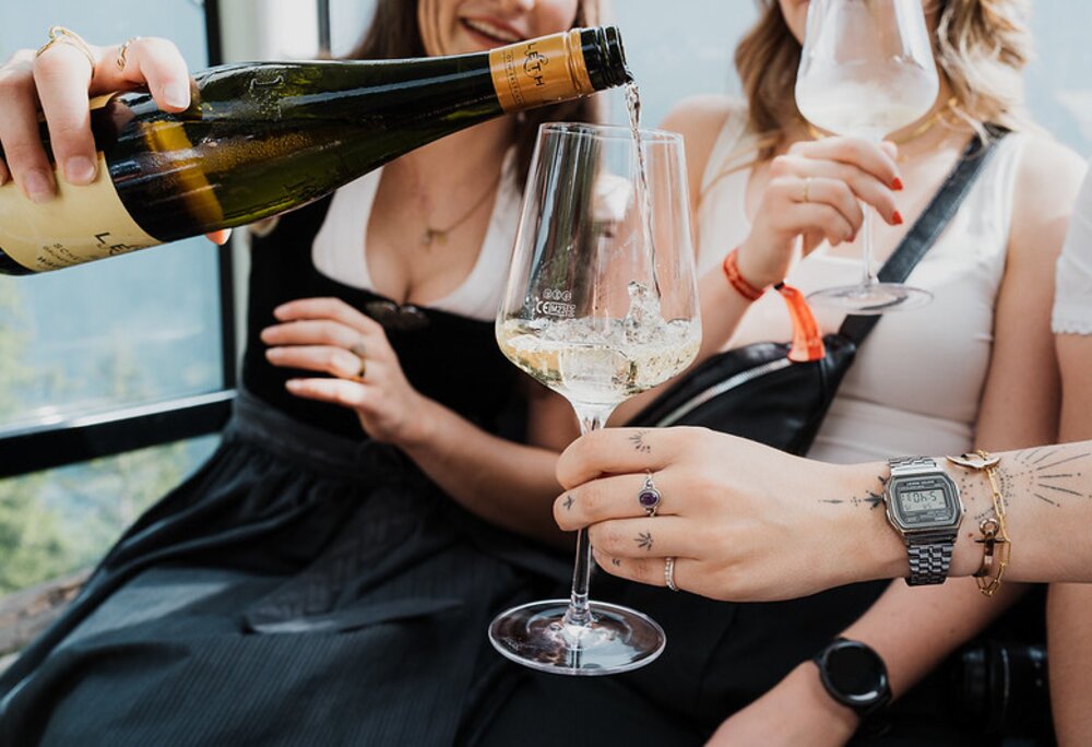 Eine junge Frau schenkt Wein in ein Weinglas in einer Gondel ein | © Silvretta Montafon - GOODGUYPAEZ