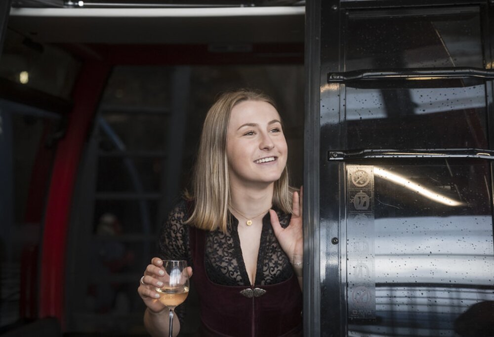 Eine junge Frau schaut mit einem Weinglas in der Hand aus der Gondel | © Silvretta Montafon - Ruth Barthold
