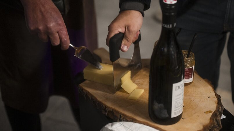 Eine Flasche Wein udn ein Käse auf einem Käsebrett der gerade angeschnitten wird | © Silvretta Montafon - Ruth Barthold